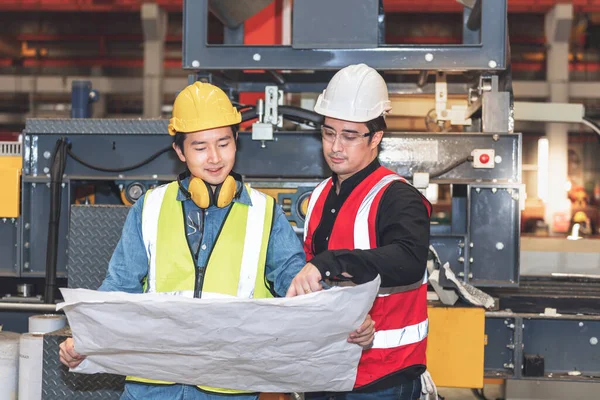 Caucasian male engineer and Asian maintenance engineer, are working and looking at blueprint, Consulting and planning collaboration in industrial plant, to workers teamwork and industry concept