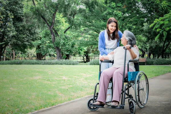 Asian family, attractive daughter looking and  taking care her mother is patient with paralysis, Sitting on a wheelchair, at green garden, to relationship in family and health care concept