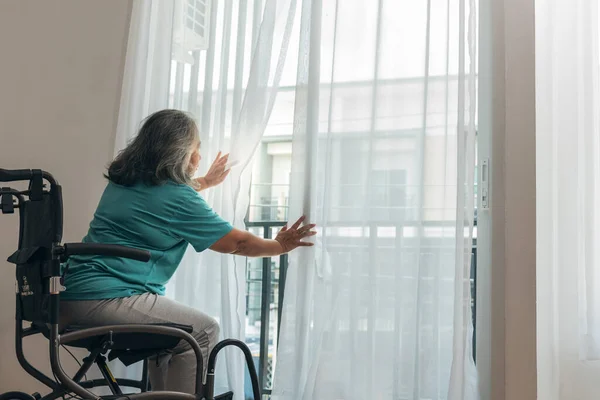 Asian elderly woman Sitting absent lonely on a wheelchair and looking outside the door,  are like waiting for the child to come home, to retirement age and health care concept.