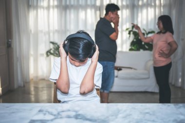 Kulaklıklarını elleriyle kapatan Asyalı genç bir çocuk, anne ve babanın tartışmalarının bulanık geçmişiyle, tartışmaların neden olduğu aile ve insan sorunlarına karşı,.