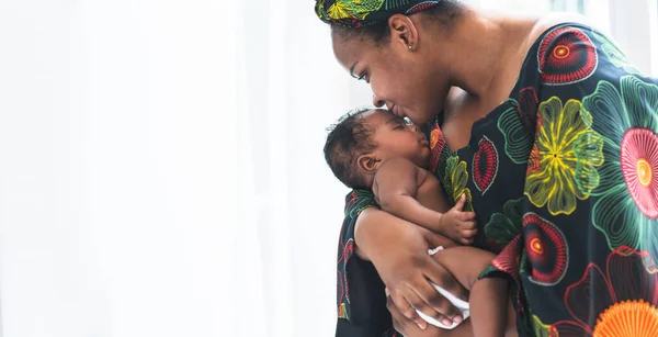 An African mother holding and kissing her son forehead, 2-month-old baby newborn which sleeping on mother\'s chest, with white background, concept to African family relationship and black skin baby newborn