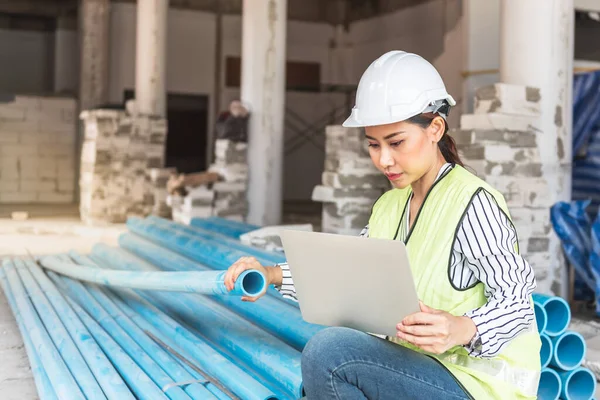 Asian woman construction engineer using notebook computer for checking the PVC pipe, to meet the standards of the work, to workers and residential building construction concept.