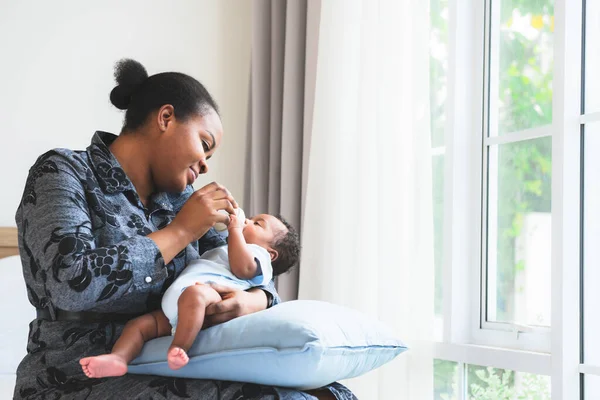 an African mother feeding milk from bottle milk to her 2-month-old baby newborn son, to African family and food for infant concept.