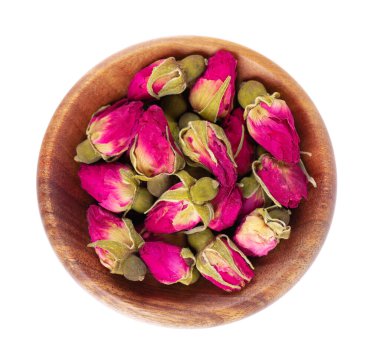 Beyaz arka planda izole edilmiş, ahşap kasede kurumuş çay gülleri tomurcukları. Gül çiçeği çayı. Kesme yolu. Üst görünüm.