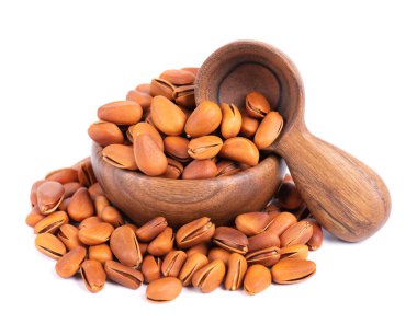 Ahşap kasede çam fıstığı ve kaşık, beyaz arka planda izole. Kavrulmuş çam fıstığı yığını..