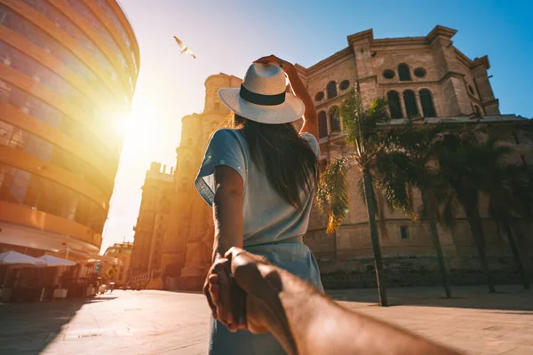 Následujte mě - POV. Mladá turistka v bílém slunečním klobouku drží svého přítele ručně a při západu slunce se prochází ve městě Malaga. Pár letních prázdnin ve Španělsku. Cestování společně. — Stock fotografie