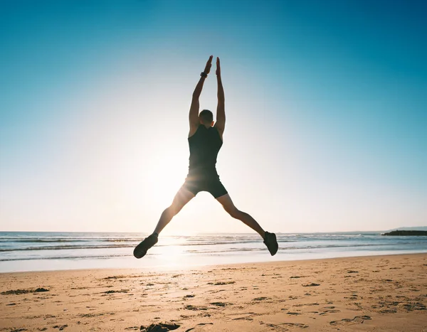Ugráló ember. Fiatal fitness férfi csinál ugró bubi vagy csillag ugrás gyakorlat a strandon — Stock Fotó