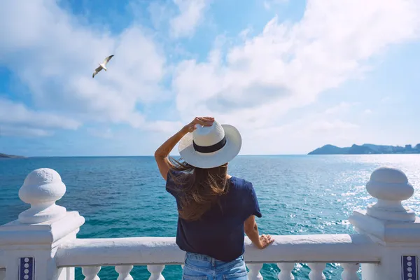 Vista posteriore della donna turista con cappello da sole godendo vista sul mare o sull'oceano. Vacanze estive — Foto Stock