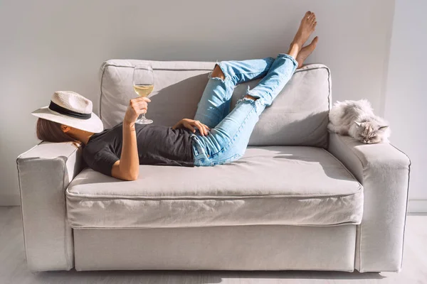 Mujer joven con copa de vino blanco descansando en el sofá en casa. Mujer disfrutando de tiempo libre y fin de semana perezoso. —  Fotos de Stock
