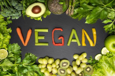  Top view of fresh green vegetables and fruits frame with word vegan on a black background. Vegan food and vegan diet concept