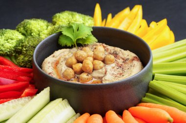 Tasty chickpeas hummus in black plate with fresh vegetables and smoked paprika