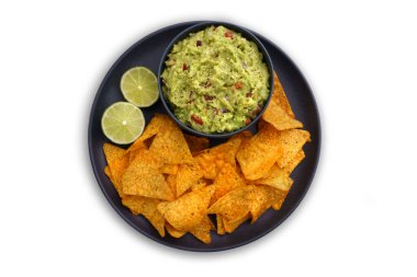 Beyaz arka planda izole edilmiş tortilla cipsi ya da nachos ile siyah tabağa batırılmış guacamole sosunun üst görüntüsü