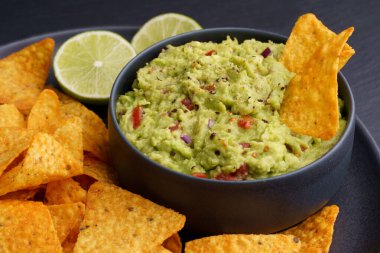 Tortilla cipsli guacamole sosu ya da siyah arka planda siyah tabakta nachos.
