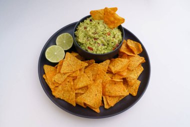 Beyaz arka planda izole edilmiş siyah tabakta Guacamole sosu ve tortilla cipsi veya nachos.