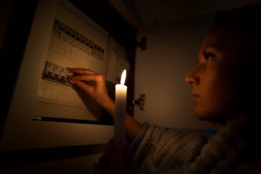 Elektrik kesintisi ya da elektrik kesintisi sırasında evdeki sigorta kutusunu araştıran tamamen karanlıkta bir kadın. Elektrik konsepti yok