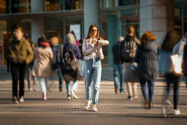 Mujer joven caminando en el medio de la calle llena de gente y mirando el tiempo a la mano relojes. Vida en la gran ciudad. — Foto de Stock