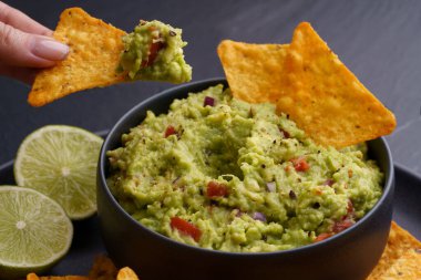 Tortilla cipsli kadın eli ya da siyah arka planda siyah tabağa taze guacamole soslu nachos.