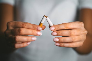 Sigarayı bırak, sigarayı bırak ya da sigara içme. Elinde kırık sigara tutan bir kadın. Sigara içmeyi reddeden kadın. Kötü alışkanlığı bırak..