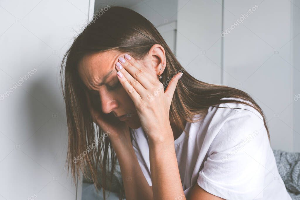 Young woman touching her temples and suffering from head pain, headache or migraine after waking up