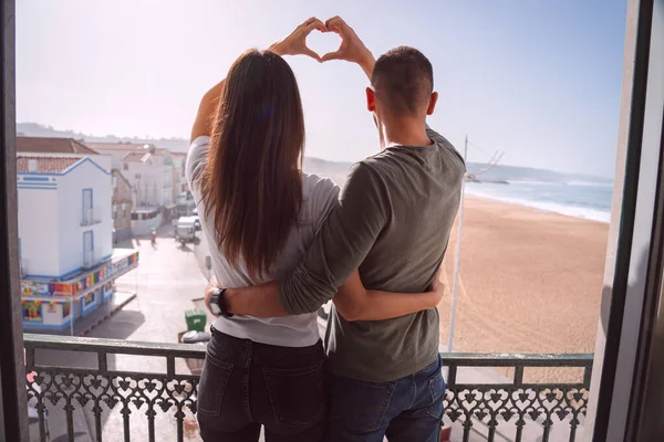 Mladý pár stojí na balkóně a rukama vytváří tvar srdce. Pár v lásce objímání a trávení Valentýna spolu — Stock fotografie