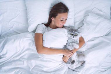 Güzel bir kadın yatakta uzanıyor ve sevimli kedisine sarılıyor. Kedileri severim. İnsanlar ve hayvanlar sevgi ve güven