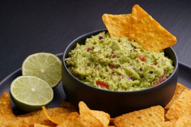 Tortilla cipsli guacamole sosu veya siyah arka planda cips ve limon.