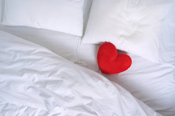 Vista superior de la cama blanca, almohadas y juguete corazón rojo — Foto de Stock