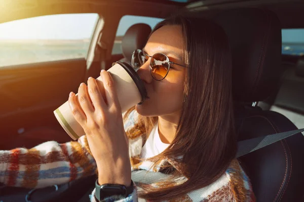 Ung vacker kvinna som kör bil och dricker kaffe. — Stockfoto