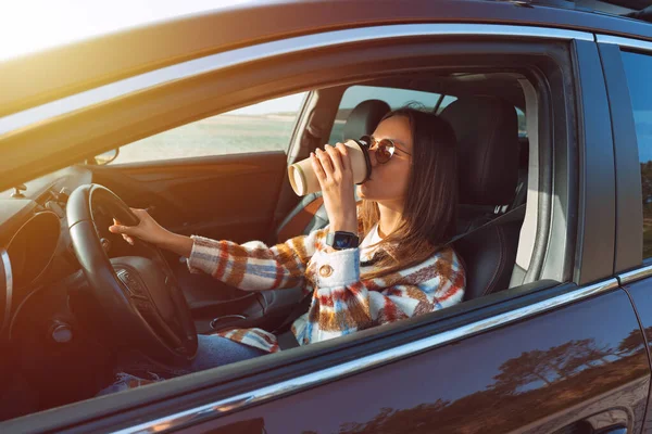 Νεαρή όμορφη κομψή γυναίκα οδήγηση νέο αυτοκίνητο της και πίνοντας καφέ σε μια ηλιόλουστη μέρα. Concept για ενοικίαση αυτοκινήτου — Φωτογραφία Αρχείου