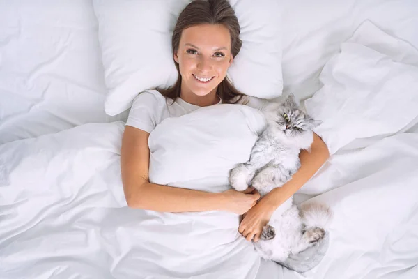 Hermosa mujer acostada en la cama y abrazando a su precioso gato lindo. Durmiendo con gato —  Fotos de Stock