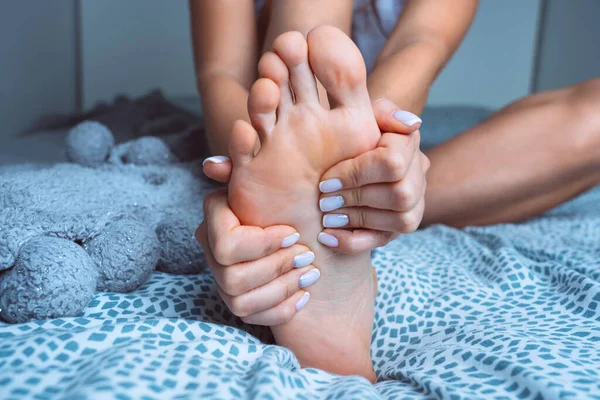 Женщина массирует усталую болезненную ногу в постели. Боль в ногах, судороги, боль в ногах или мышечный спазм — стоковое фото