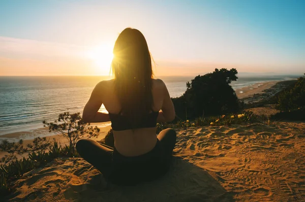 Woman practicing yoga and meditates on the mountain with ocean view at sunset. Young woman sitting in lotus pose outdoor in the nature — Foto Stock