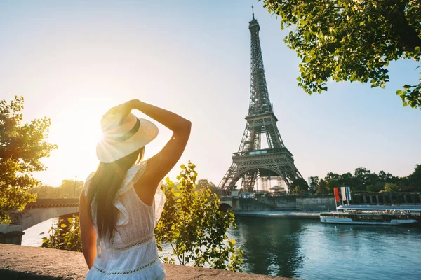 夕暮れ時にパリのエッフェル塔の前に立つ太陽の帽子と白いドレスの若い女性観光客 フランスの旅行 観光の概念 高品質の写真 ストック画像