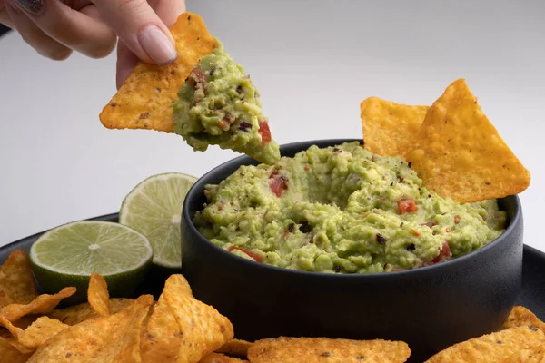 Closeup of woman hand with tortilla chip or nachos with tasty guacamole dip. High quality photo