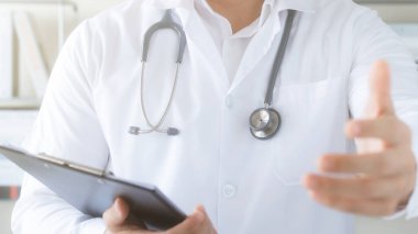 Erkek doktor kendini tanıtıyor ve hastaneye kabul edilen hastaları kabul ederken elini uzatıyor. Hastalara selamlarını ve tebriklerini iletiyor..