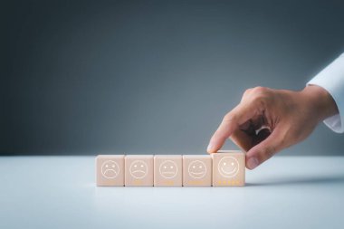 Customer satisfaction survey concept, customer hand selects wooden cube with smiley face icon, best service excellence rating for satisfaction.	