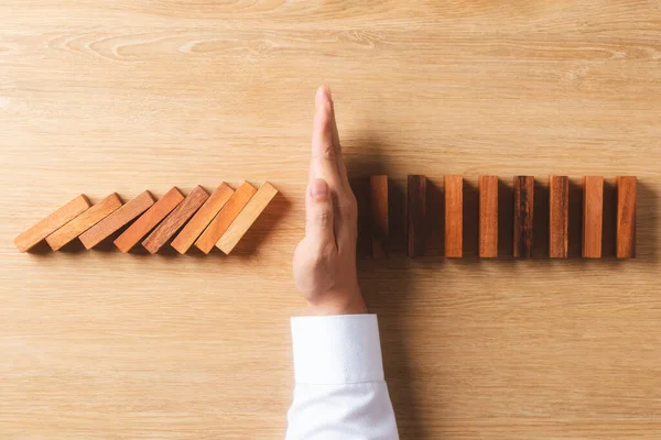 Risk management and business strategy concept, businessman hands stop the dominoes from falling continuously, preventing future risks from crisis.