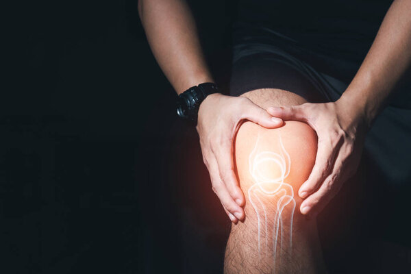 Young man with knee pain, joint pain, arthritis and tendon problems  exercise injury on dark background.