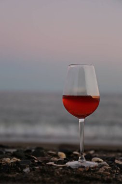 Bir bardak kırmızı şarap ve tropikal bir yaz akşamında deniz kenarında pembe bir günbatımı.