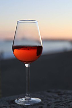 Bir bardak kırmızı şarap ve deniz kenarında pembe bir gün batımı.