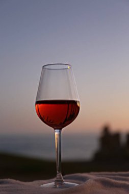 Bir bardak kırmızı şarap ve deniz kenarında pembe bir gün batımı.