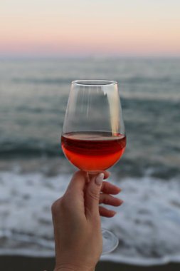 Bir bardak kırmızı şarap ve deniz kenarında pembe bir gün batımı.