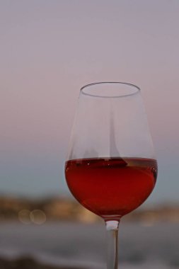Bir bardak kırmızı şarap ve deniz kenarında pembe bir gün batımı.