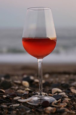 Bir bardak kırmızı şarap ve deniz kenarında pembe bir gün batımı.