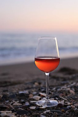 Bir bardak kırmızı şarap ve deniz kenarında pembe bir gün batımı.