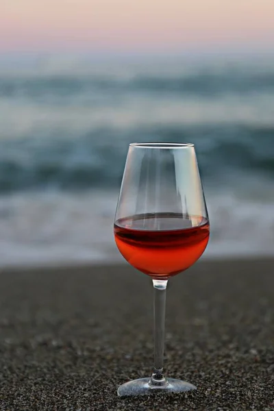 a glass of red wine and a pink sunset by the sea on a summer evening