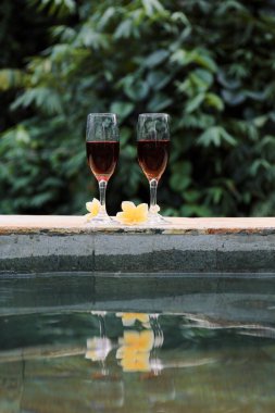 Tropiklerde yüzme havuzunun yanında kırmızı şarap bardakları