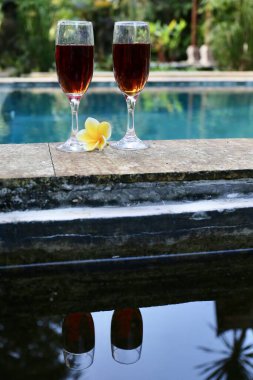 Tropiklerde yüzme havuzunun yanında kırmızı şarap bardakları