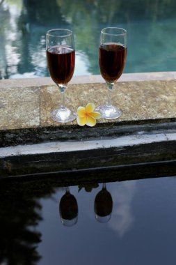 Tropiklerde yüzme havuzunun yanında kırmızı şarap bardakları