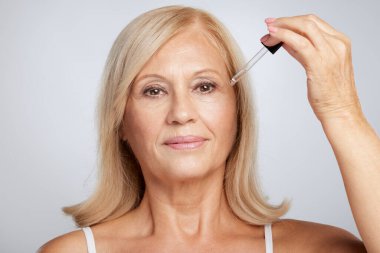 Sarışın, yaşlı bir bayan yeni bir serum deniyor. Güzellik fotoğrafçılığı